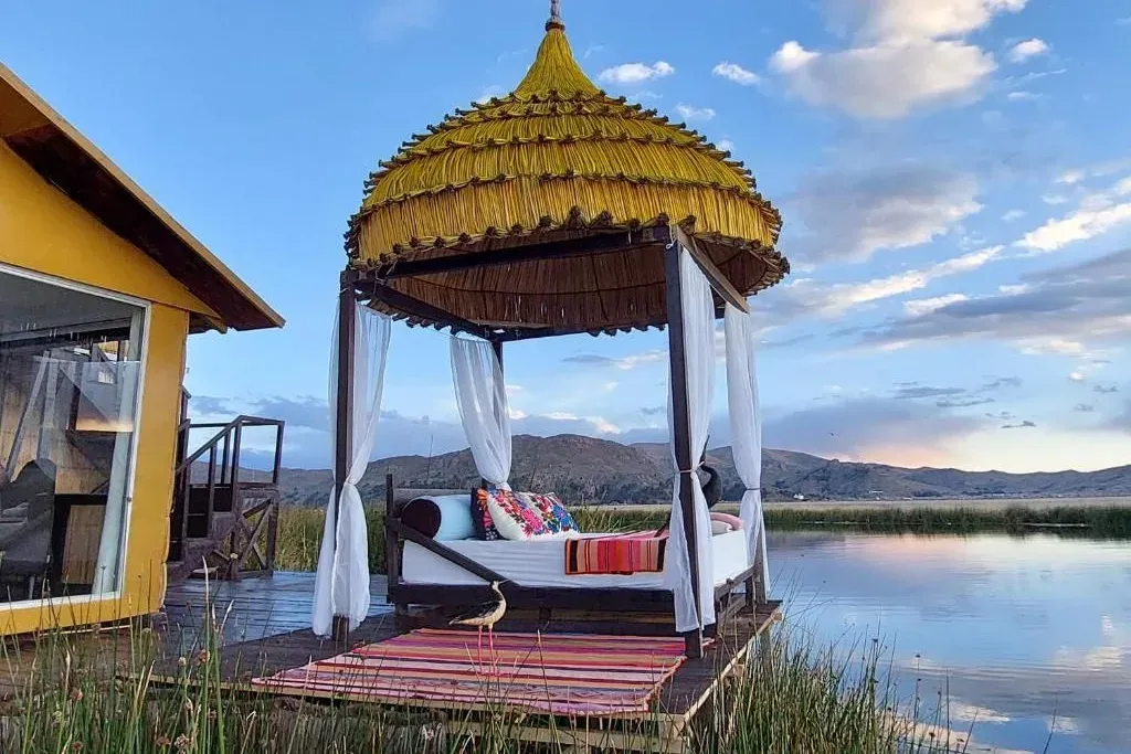 Cama con dosel de totora sobre una plataforma junto al lago