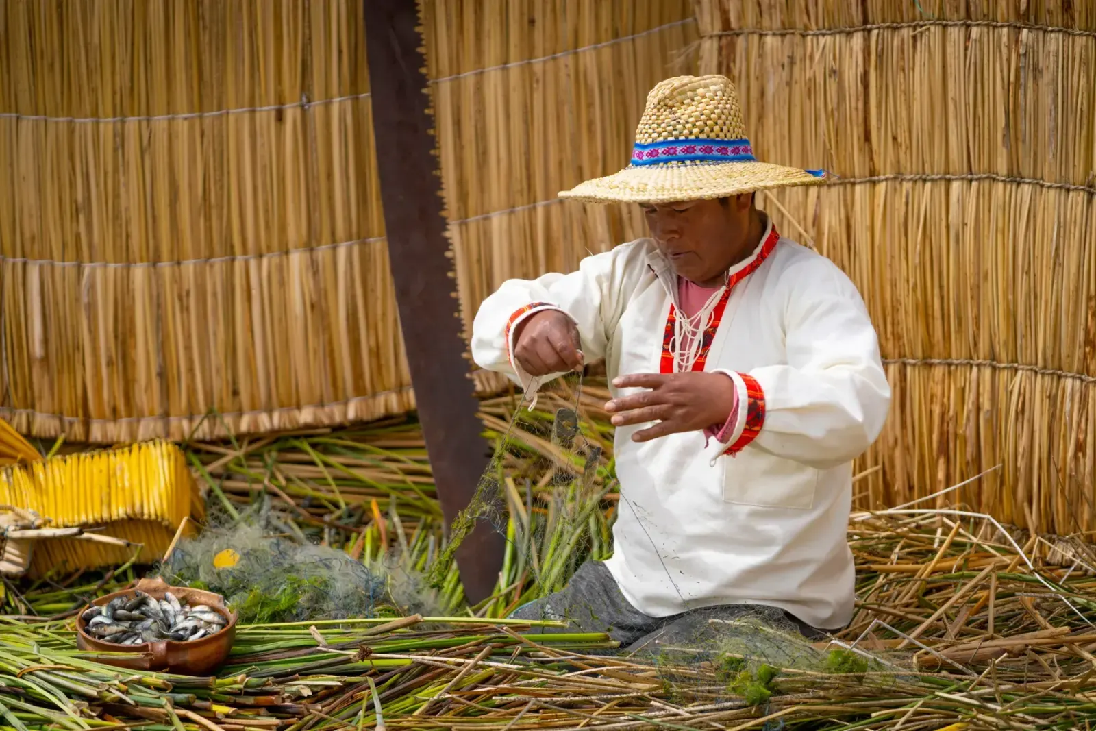 Pescador uro desenredando la red junto a un cuenco de pejerreyes
